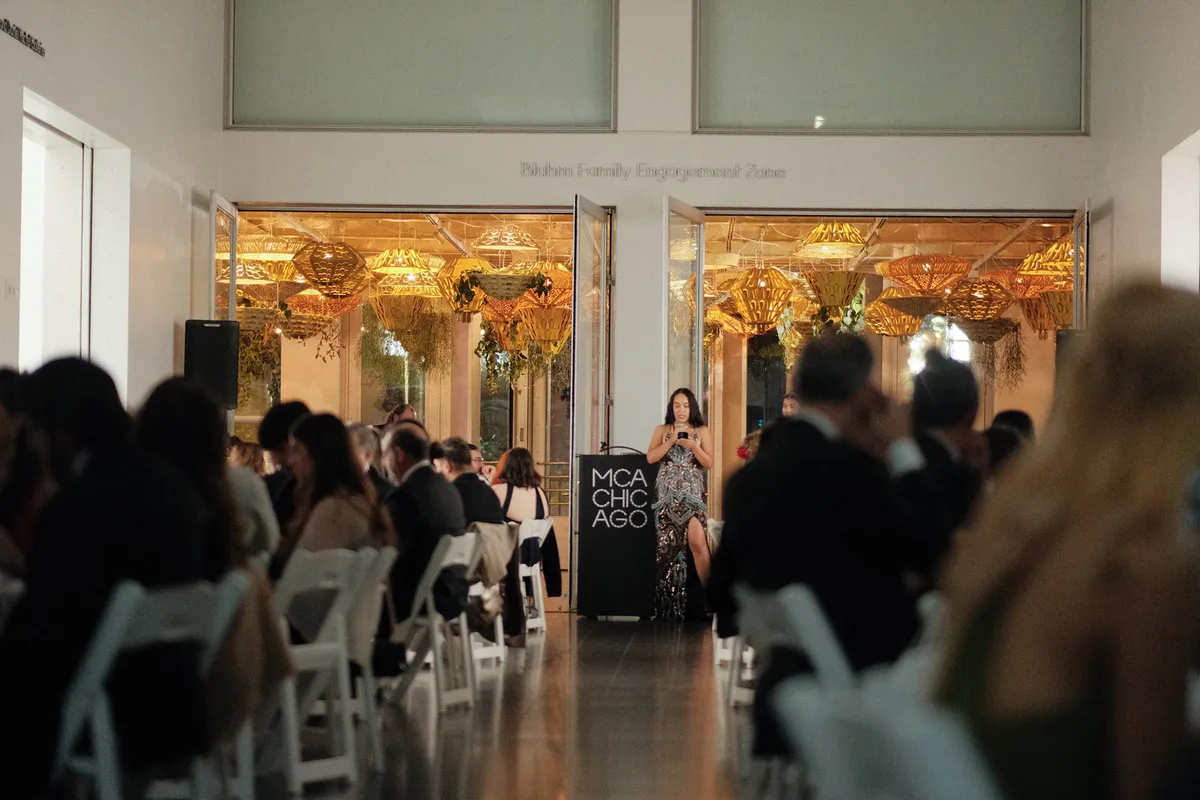 The Annual Gala 2026 dinner at MCA Chicago, tables leading to the podium beneath glowing gold lanterns