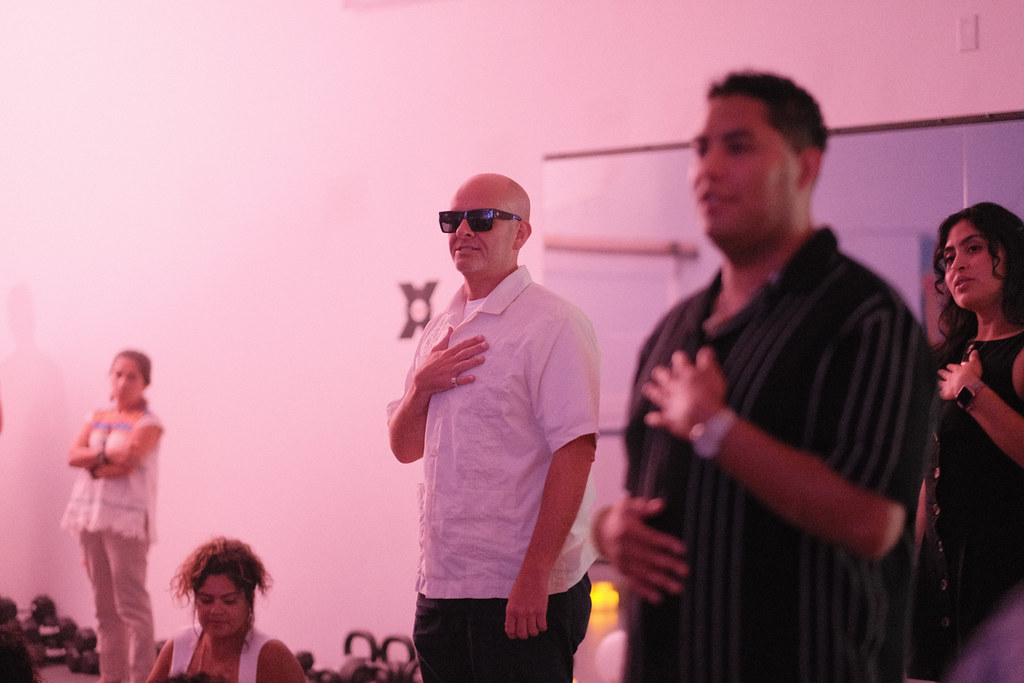 Guests standing along the studio wall with hands pressed over their hearts, kettlebells stacked on the floor behind them.